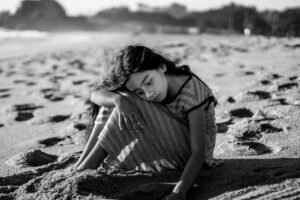 image of a little girl sat on a beach alone, absently digging a pit in the sand